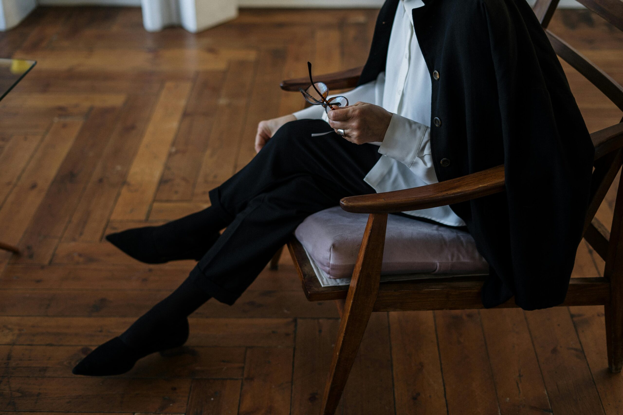 A woman holding glasses, seated indoors, exuding professionalism and calm.