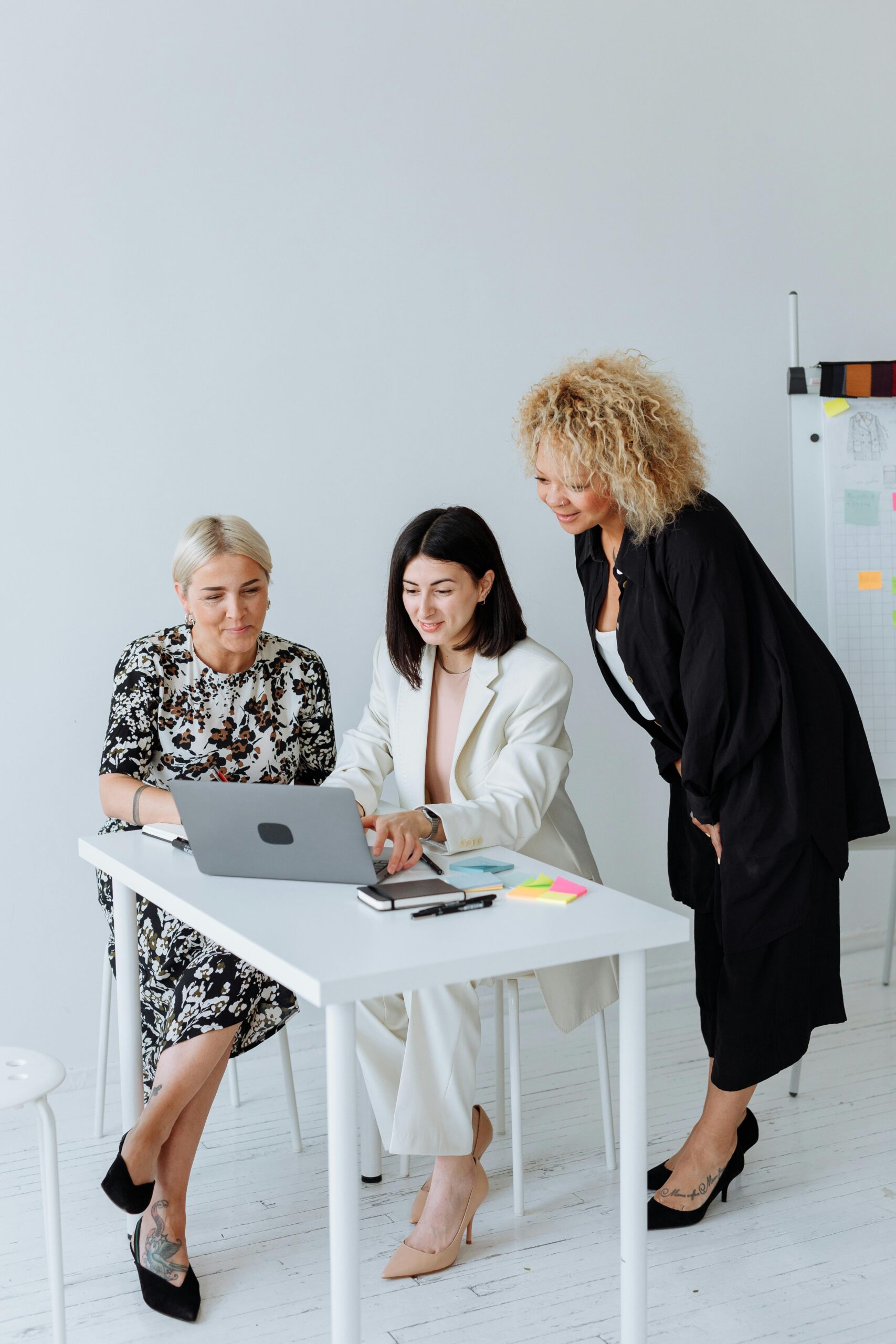 Three diverse women working together at a white table in an office setting.